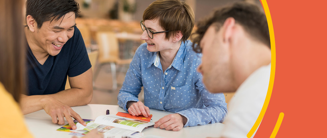 Studierende sitzen mit Beraterin zusammen an einem Tisch und unterhalten sich angeregt