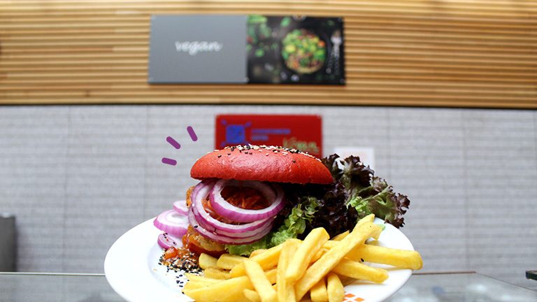 Veganer Burger mit Pommes und Salat vor dem veganen Schalter der Mensa am Park